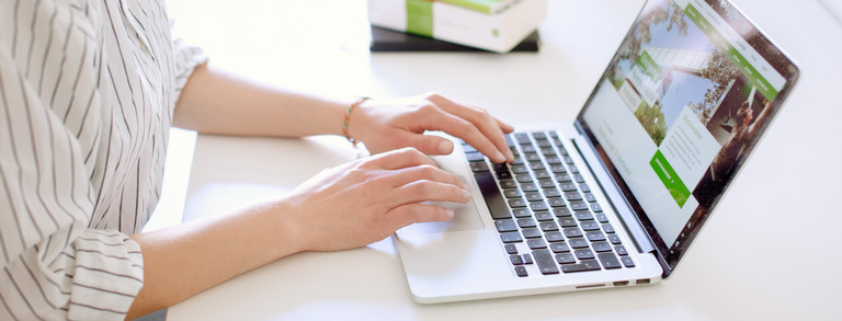 Studentin tippend am Laptop, daneben liegen Bücher.